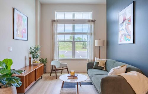spacious living room with decor, art, open windows of natural light, sofa, table and an entertainment center at new apartments in Peabody, MA at Alexan Peabody.